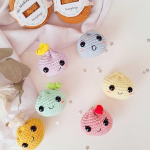 Könnte beinhalten: Eine Sammlung von sechs kleinen, runden, gehäkelten Knödel-Spielzeugen in verschiedenen Pastellfarben wie Lavendel, Hellblau, Minzgrün, Blassgelb und Rosa. Jeder Knödel hat schwarze Sicherheitsaugen aus Kunststoff, aufgestickte Lächeln und kleine dekorative Garnaufsätze.