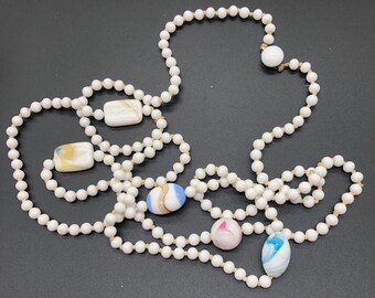 May include: A white pearl necklace with five colorful glass beads. The beads are in various shapes and sizes, including squares, ovals, and circles.