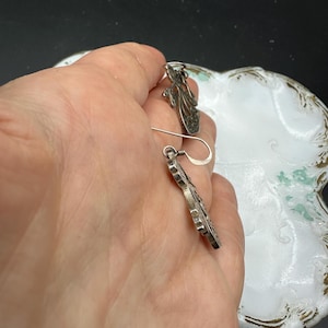 May include: A pair of silver filigree earrings with a floral design. The earrings are dangling and have a hook fastening.