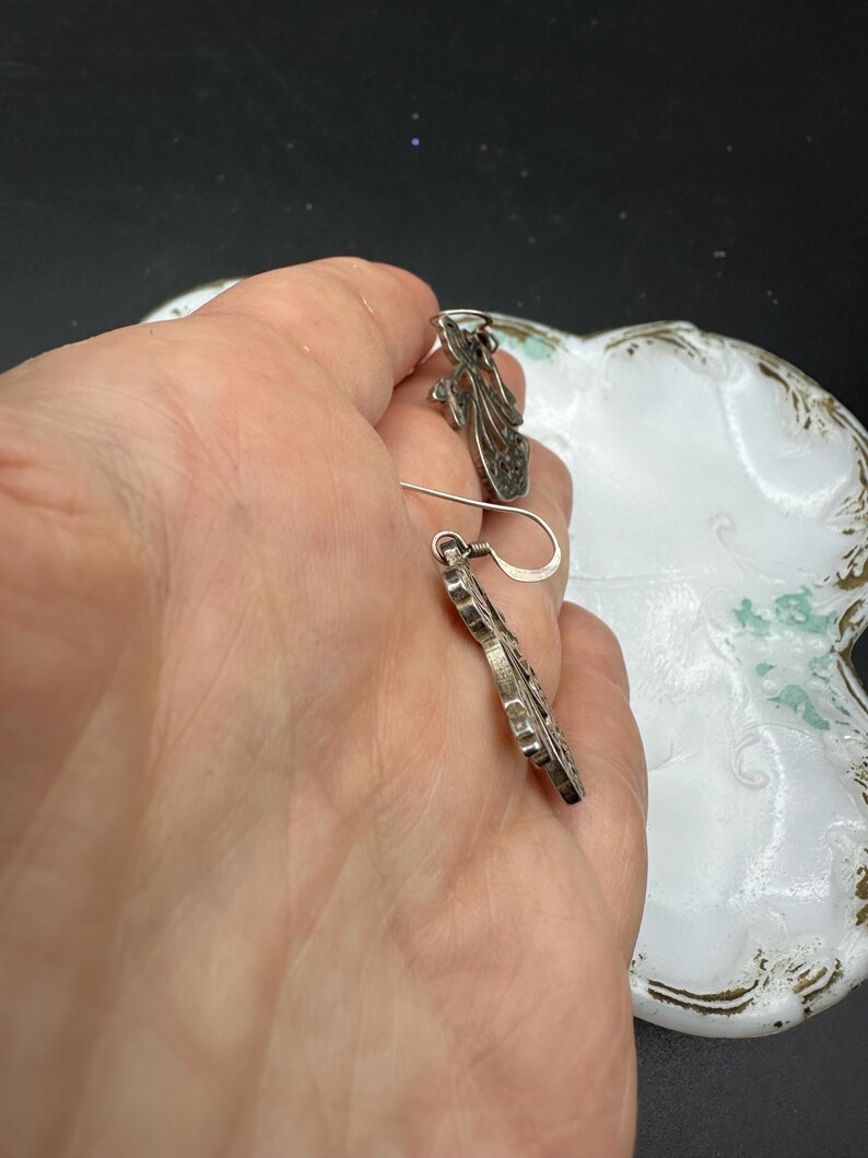 May include: A pair of silver filigree earrings with a floral design. The earrings are dangling and have a hook fastening.