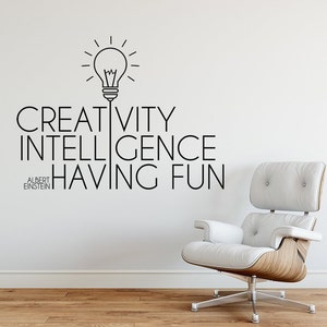 May include: A white wall with a black and white graphic of a light bulb with the text "CREATIVITY INTELLIGENCE HAVING FUN" and the quote "ALBERT EINSTEIN" below. A white leather armchair with a wooden base is in the foreground.