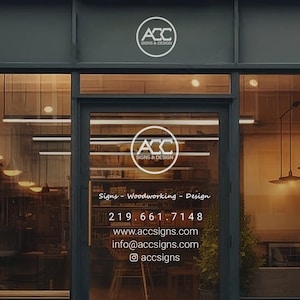 May include: A storefront with a glass door and windows. The door has a white logo with the text "ACC SIGNS & DESIGN" and the phone number "219.661.7148". The text "Signs - Woodworking - Design" is also on the door. The website address "www.accsigns.com" and email address "info@accsigns.com" are listed below the phone number. The text "@accsigns" is on the bottom of the door.