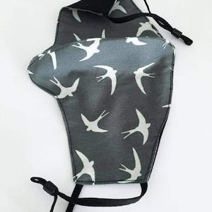 May include: A grey face mask with a white swallow pattern. The mask has black adjustable straps.