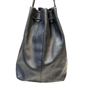 May include: A black leather drawstring bag with a shoulder strap. The bag has a rounded shape and a drawstring closure at the top. The leather appears to be slightly distressed, giving it a vintage look.