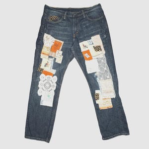 May include: Dark wash denim jeans with decorative patches. Patches include floral, lace, and animal print fabrics in white, orange, and brown. The jeans have a classic five-pocket design.