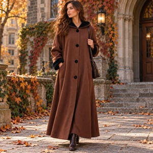May include: A long, brown, floor-length coat featuring a hood with a black interior lining, long sleeves with black cuffs, and a front button closure with four large black buttons. The coat is worn with a dark brown shoulder bag and dark boots.