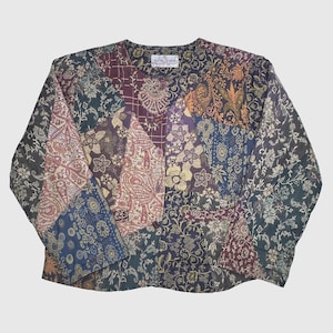 May include: A patchwork long-sleeve top featuring a variety of floral and paisley patterns in shades of blue, burgundy, gold, and green. The top has a round neckline and a button closure. The fabric appears to be lightweight.