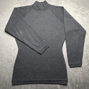 May include: A charcoal gray long-sleeve sweater featuring a mock neck collar and raglan sleeves. The garment is crafted from a fine-knit fabric with a consistent texture throughout, finished with ribbed cuffs and a matching ribbed hemline.