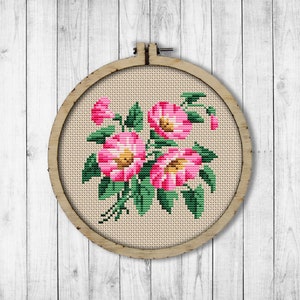 May include: A framed cross-stitch embroidery featuring a bouquet of pink flowers with green leaves on a beige background.