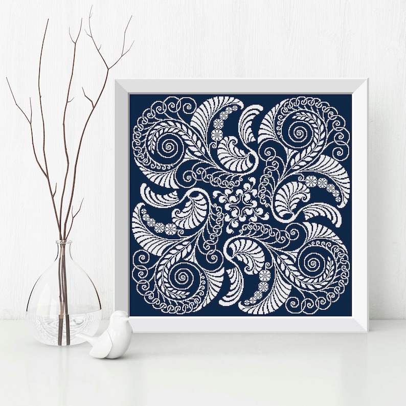 Op de afbeelding: Een ingelijst afdruk met een wit bloemenontwerp op een donkerblauwe achtergrond. Het ontwerp bevat ingewikkelde swirls en bladeren.