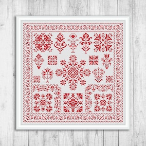 May include: A white cross-stitch sampler with a red floral and geometric design. The sampler is framed in a white frame and has a white background.