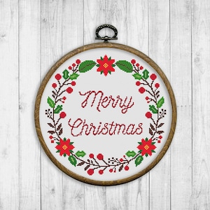 May include: A white embroidery hoop with a red and green Christmas wreath design. The wreath features poinsettia flowers, berries, and leaves. The text "Merry Christmas" is embroidered in red in the center of the wreath.