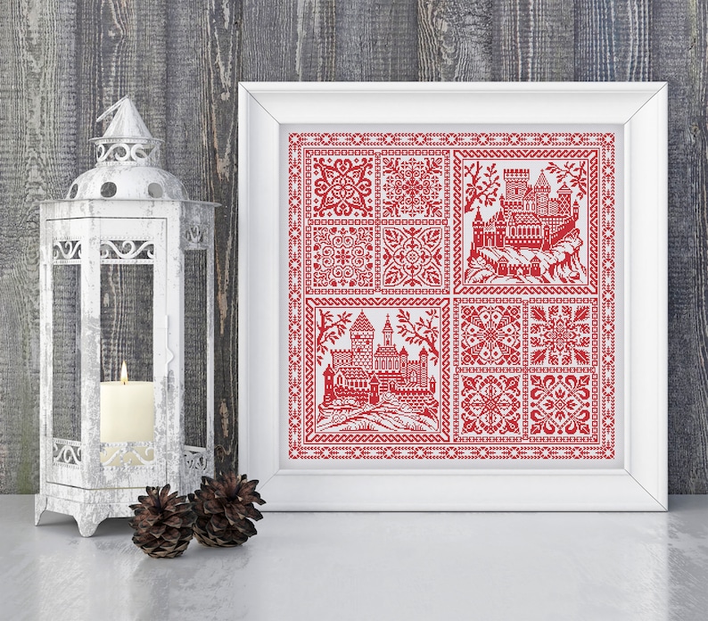 May include: A framed cross-stitch design featuring a red castle and floral patterns. The design is stitched on white fabric and framed in a white frame.