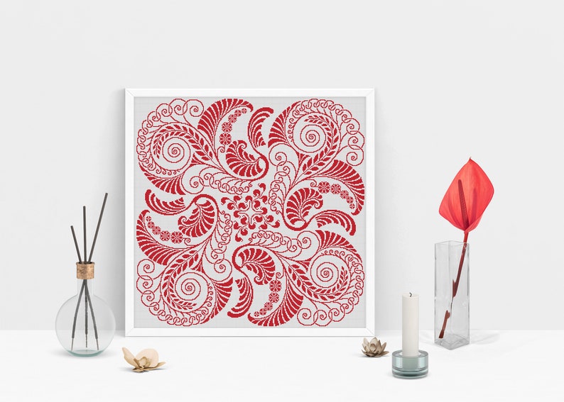 Op de afbeelding: Een ingelijst rood en wit kruissteekpatroon met een bloemmotief. Het ontwerp bevat draaiende bladeren en bloemen.
