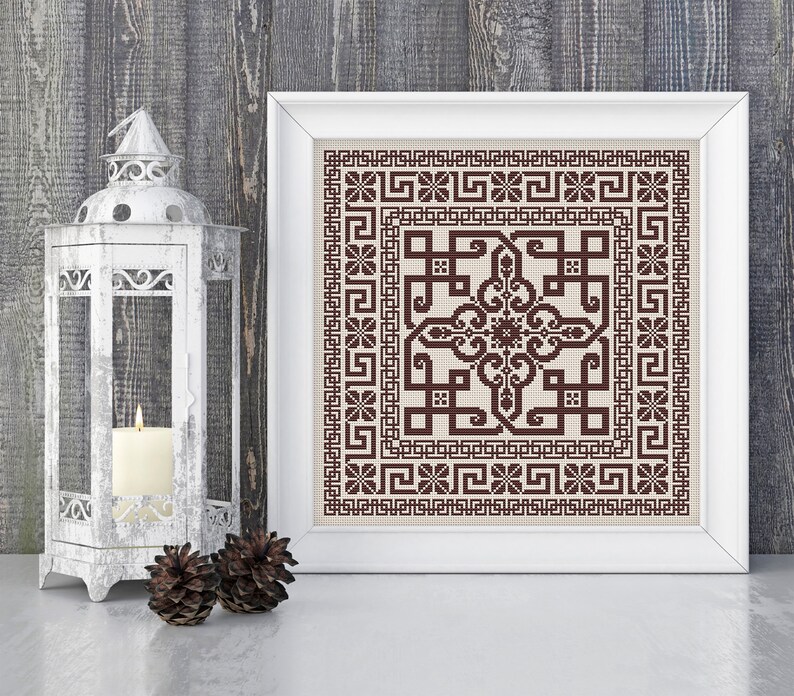 May include: A framed cross-stitch embroidery with a brown geometric pattern on a beige background. The frame is white and the embroidery is in a square shape.