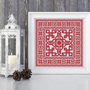 May include: A white framed picture with a red and white cross-stitch design. The design features a geometric pattern with a central motif.
