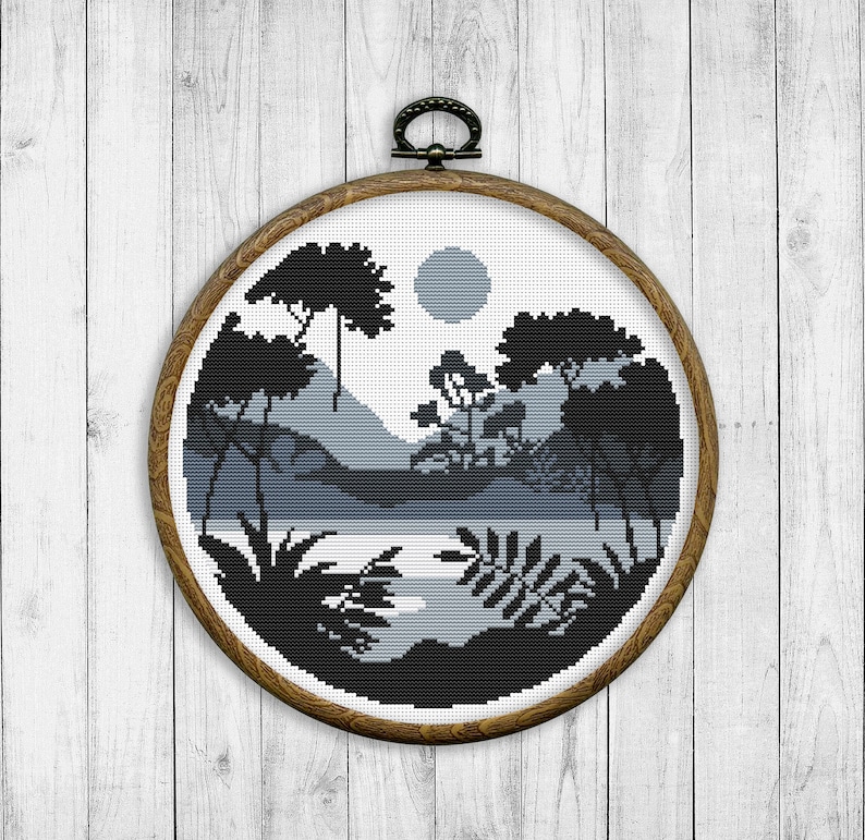 May include: A black and white cross-stitch embroidery of a landscape scene with trees, mountains, and a lake. The embroidery is framed in a round wooden hoop.
