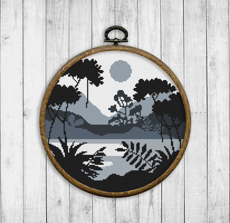 May include: A black and white cross-stitch embroidery of a landscape with trees, mountains, and a lake. The embroidery is framed in a round wooden hoop.