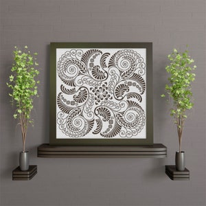 Op de afbeelding: Een ingelijst zwart-witdruk van een decoratief bloemmotief met ingewikkelde spiralen en bladeren. De print hangt aan een muur met een bruine baksteenstructuur.