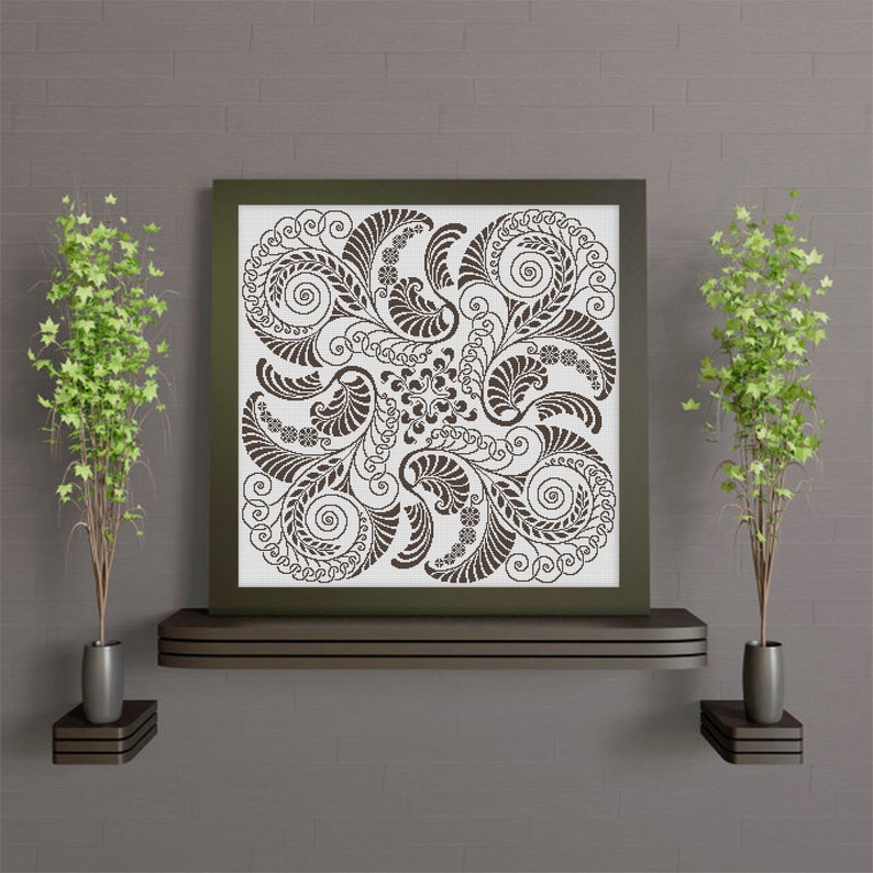 Op de afbeelding: Een ingelijst zwart-witdruk van een decoratief bloemmotief met ingewikkelde spiralen en bladeren. De print hangt aan een muur met een bruine baksteenstructuur.