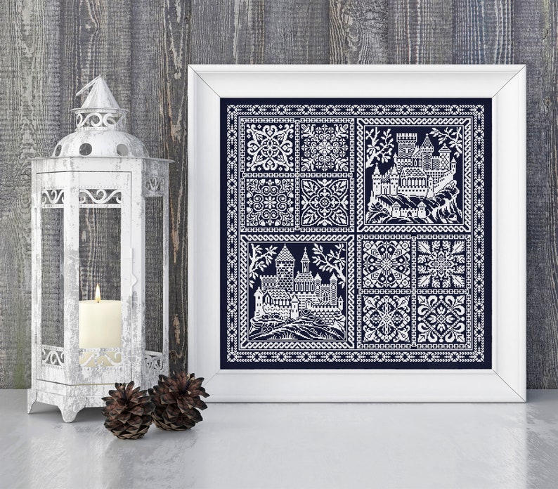 May include: A framed cross-stitch embroidery featuring a white castle design on a dark blue background. The design is divided into nine squares, with the castle in the centre and various geometric patterns in the surrounding squares.