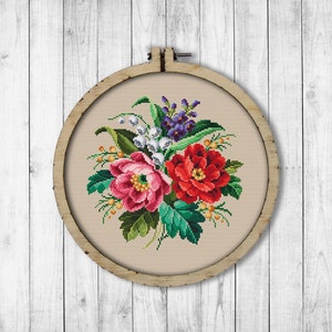 May include: A framed cross-stitch embroidery featuring a bouquet of pink, red, and white flowers with green leaves. The flowers are arranged in a circular pattern and are surrounded by a brown wooden frame.