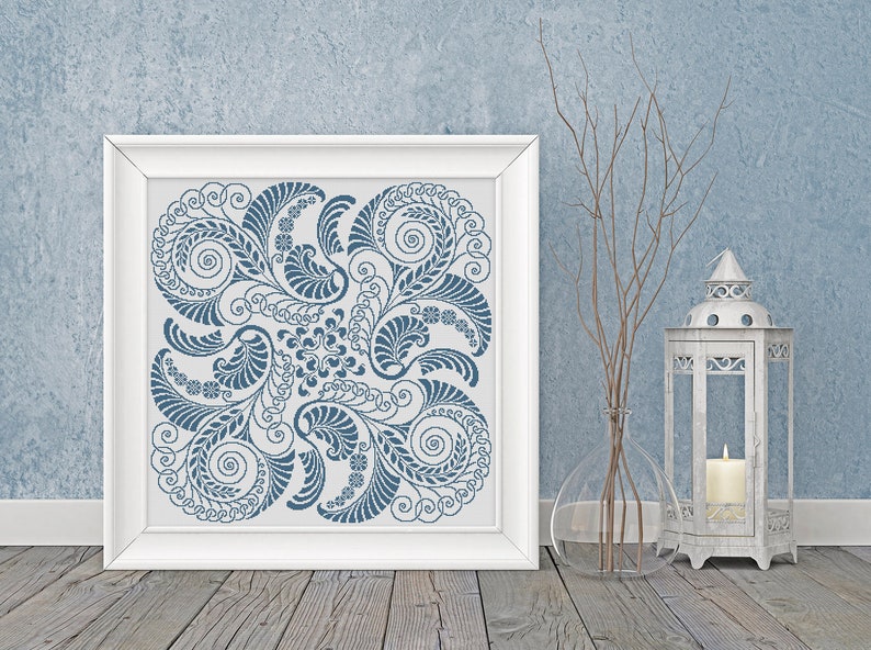 Op de afbeelding: Een wit frame met een blauw en wit bloemenontwerp op een witte achtergrond. Het frame staat op een houten vloer met een vaas en een lantaarn op de achtergrond.