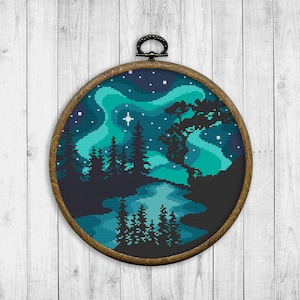 May include: A round wooden embroidery hoop with a cross-stitch design of a forest scene under a blue and green aurora borealis. The design includes a lake, trees, and stars.