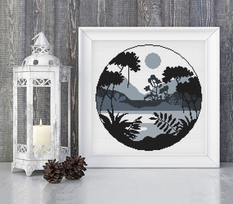 May include: Black and white cross stitch pattern of a circular landscape with trees, mountains, and a lake. The design is framed in a white frame.