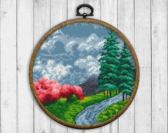 May include: A round wooden embroidery hoop featuring a cross-stitch design of a landscape with a river, trees, and flowers. The sky is blue with white clouds.