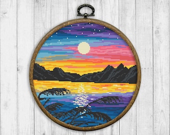 May include: A colourful cross-stitch embroidery depicting a sunset over a body of water with palm trees in the foreground. The embroidery is framed in a round wooden hoop.