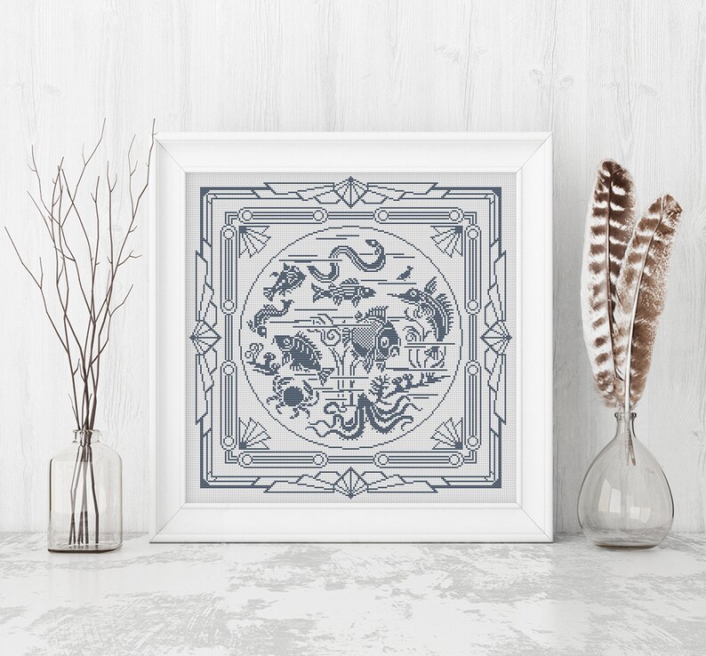 May include: A framed cross-stitch design featuring a circle of various sea creatures, including fish, a crab, an octopus, and a seahorse. The design is surrounded by a geometric border in a light blue color.