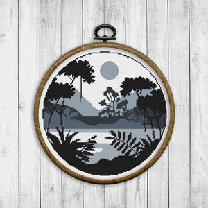 May include: A black and white cross-stitch embroidery of a forest scene with a moon in the sky. The embroidery is framed in a brown wooden hoop.