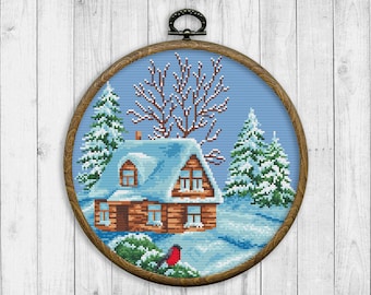 May include: A framed cross-stitch embroidery showing a winter scene with a small brown cottage covered in snow, surrounded by pine trees and a red bird.