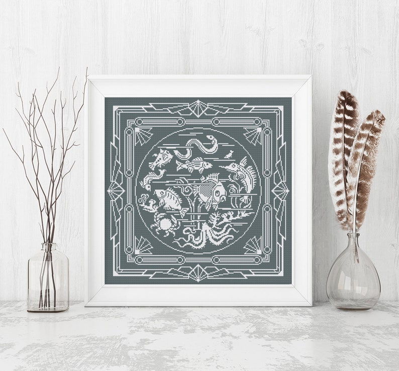May include: A framed cross-stitch design featuring a gray background with a white outline of a circle filled with various fish, a crab, an octopus, and seaweed. The circle is surrounded by a geometric pattern.