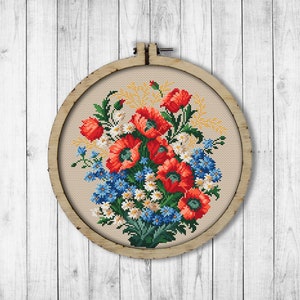 Może przedstawiać: Haftowany krzyżykiem bukiet czerwonych maków, niebieskich niezapominajek i białych stokrotek w drewnianym obręczy do haftu.