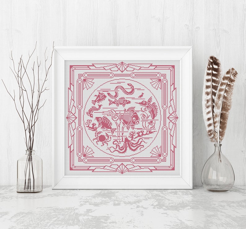 May include: A framed cross-stitch design featuring a pink and white geometric pattern with a circle in the center. The circle contains a variety of pink fish, sea creatures, and plants.