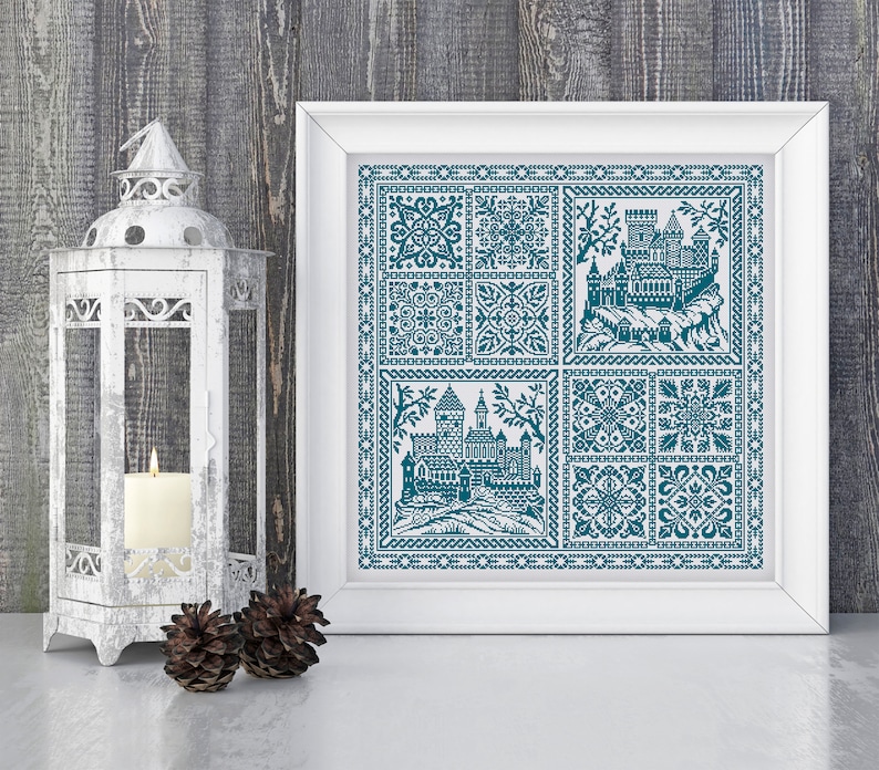 May include: A framed cross-stitch design featuring a blue and white castle scene with intricate floral patterns. The castle is surrounded by a border of small squares and the design is framed in white.