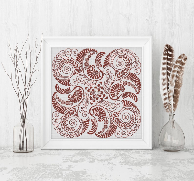 Op de afbeelding: Een vierkante ingelijste print met een bruin bloemenontwerp op een witte achtergrond. Het ontwerp is symmetrisch en bevat ingewikkelde swirls en bladeren.