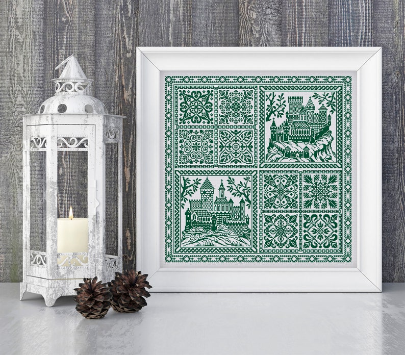 May include: A framed green and white cross-stitch embroidery featuring a castle and floral designs. The embroidery is in a white frame with a white mount.