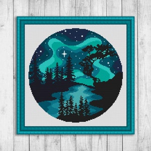 Op de afbeelding: Een kruissteekpatroon met een donkerblauwe en groene nachthemel met een silhouet van een bos en een meer. De hemel is gevuld met sterren en een heldergroene aurora borealis.