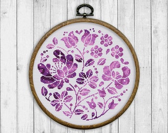 Puede incluir: Un diseño de bordado floral morado en un aro de bordado de madera redondo. El diseño presenta una variedad de flores y hojas en tonos morados.