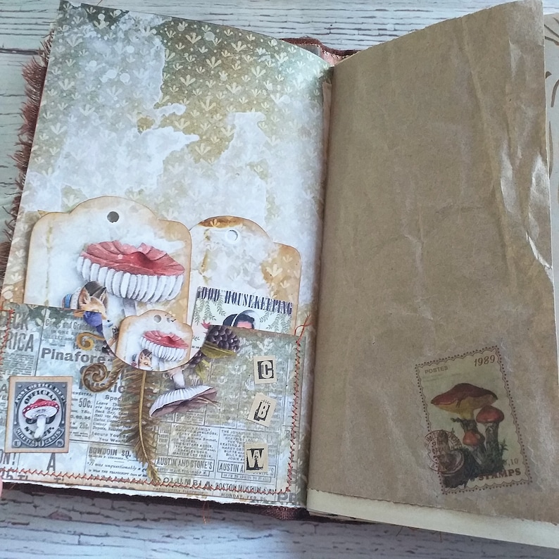 K&ouml;nnte beinhalten: Offenes Journal mit dekorierten Seiten. Es zeigt Pilz-Themen-Tags, Vintage-Ephemera und eine Briefmarke mit Pilz-Illustrationen. Das Journal hat eine rustikale, handgemachte &Auml;sthetik mit einer gen&auml;hten Bindung.