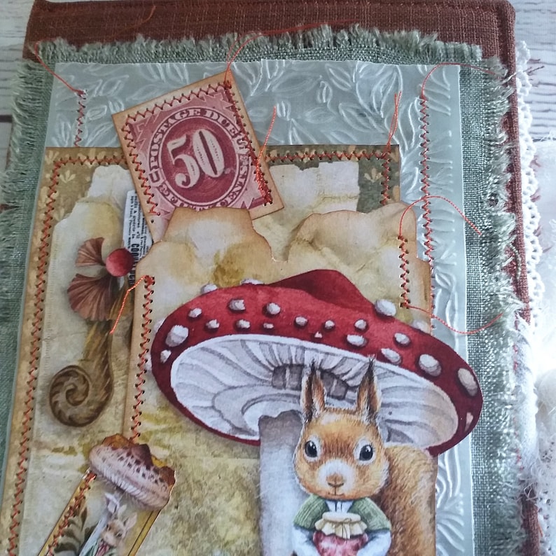 K&ouml;nnte beinhalten: Ein handgefertigtes Journal mit einem skurrilen Waldthema. Es zeigt einen rot gekappten Pilz, eine Eichh&ouml;rnchen-Illustration und eine Vintage-Briefmarke. Die Seiten sind mit dekorativen N&auml;hten und geschichteten Papierelementen verziert, was ein einzigartiges, k&uuml;nstlerisches Gef&uuml;hl erzeugt.