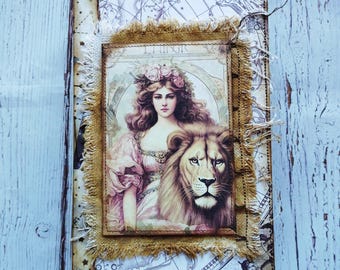 May include: A vintage-style journal with a printed image of a woman with a floral crown and a lion. The image is framed with burlap and set against a background of antique maps. The journal's cover has a distressed, aged appearance.