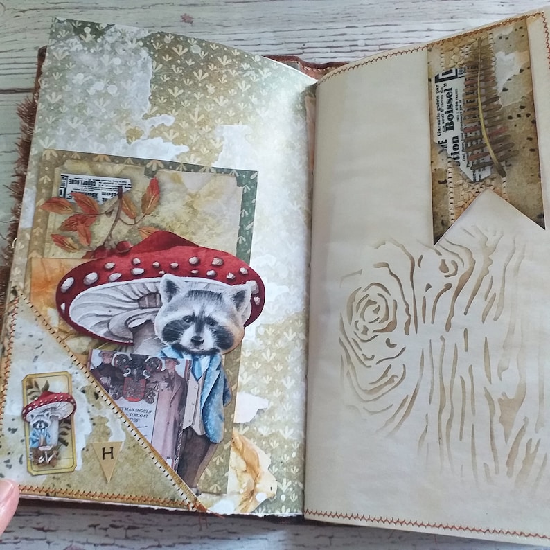 K&ouml;nnte beinhalten: Offenes Journal mit einem skurrilen Waldthema. Enth&auml;lt eine Illustration eines Waschb&auml;ren im Anzug, einen roten Pilz und Vintage-Papierelemente. Die Seiten haben eine hellbraune Farbe mit einem Baumrinden-Design.
