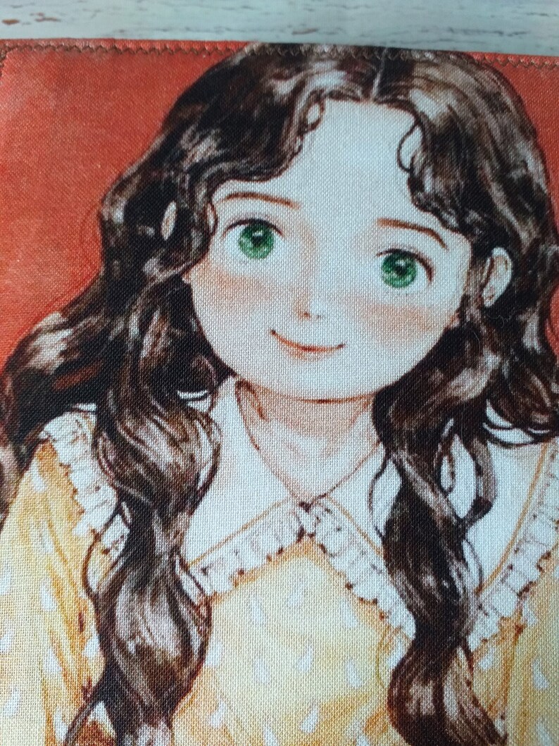 以下が含まれることがあります： 若い女性の水彩画風イラストが描かれた布製品のクローズアップ。彼女は長く、濃い色のウェーブのかかった髪、緑色の目、バラ色の頬をしています。白い水玉模様の黄色いドレスと白いレースの襟を赤い背景に着用しています。
