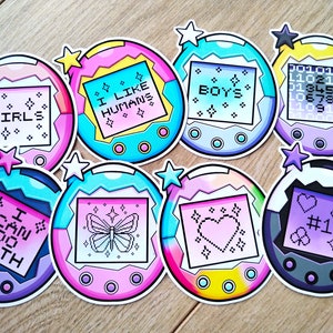 May include: Nine colourful digital pet toy stickers with various designs and text, including "GIRLS", "I LIKE HUMANS", "BOYS", "CAN DO BOTH", "#1", and a butterfly.