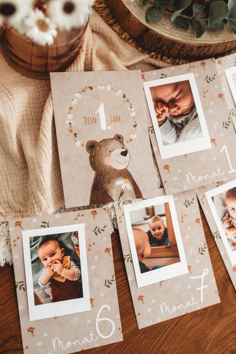 Pu&ograve; includere: Una collezione di biglietti per bambini con foto. Le carte presentano un'illustrazione di orso e le parole "Dein Jahr" e "Monat". Le carte sono decorate con motivi floreali e di foglie, e le foto sono in cornici con bordi bianchi.