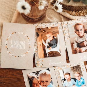 Könnte beinhalten: Ein Baby-Fotoalbum mit den Worten "LIEBLINGS MOMENTE" und floralen Akzenten. Das Album ist geöffnet und zeigt Babyfotos mit den Monaten "Januar" und "Februar" darauf. Das Album liegt auf einer Holzoberfläche.